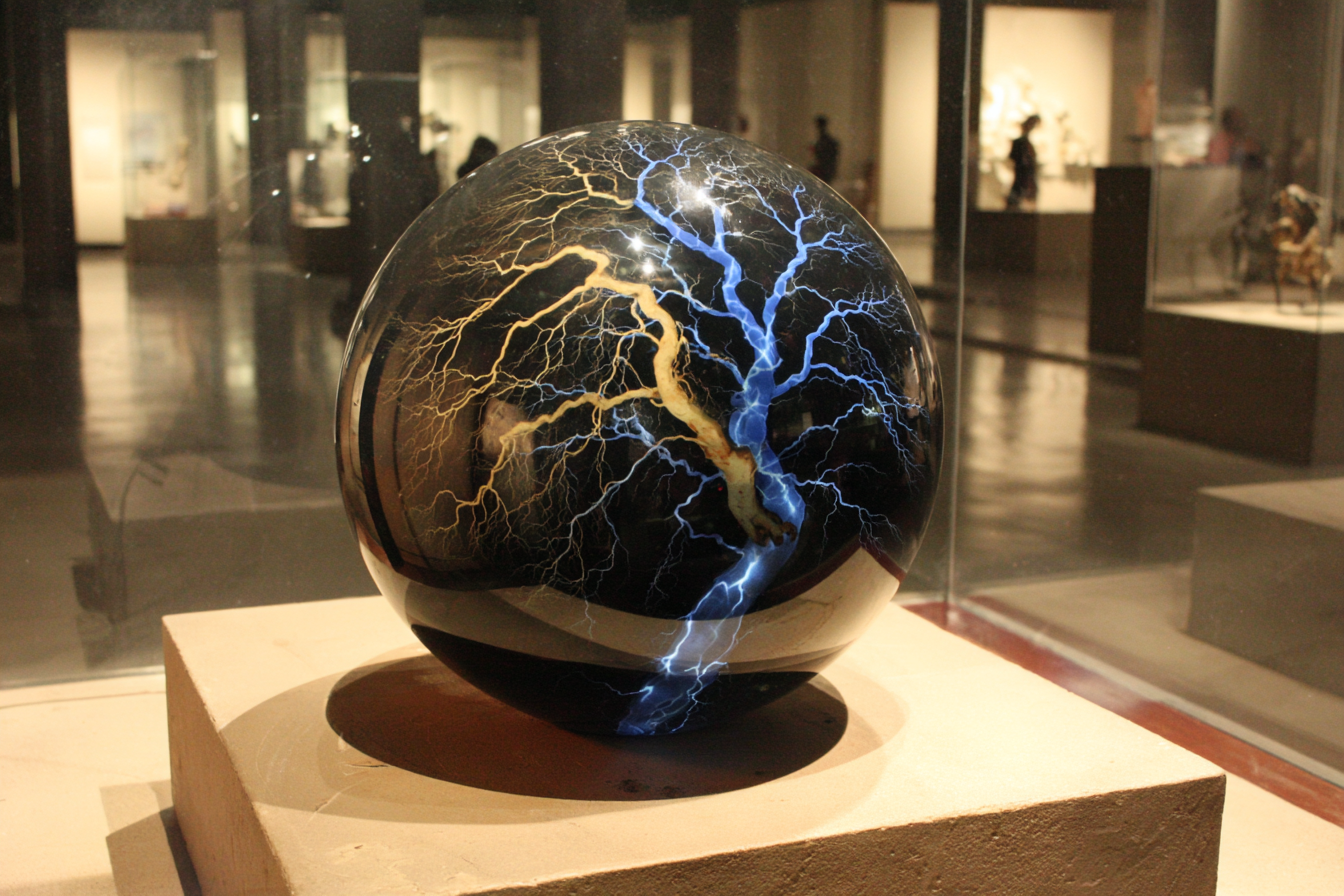 Cross-section of dark translucent glass sphere, interior shows one hemisphere dimming into shadow while the other ignites with cobalt-blue bioluminescent filaments branching outward