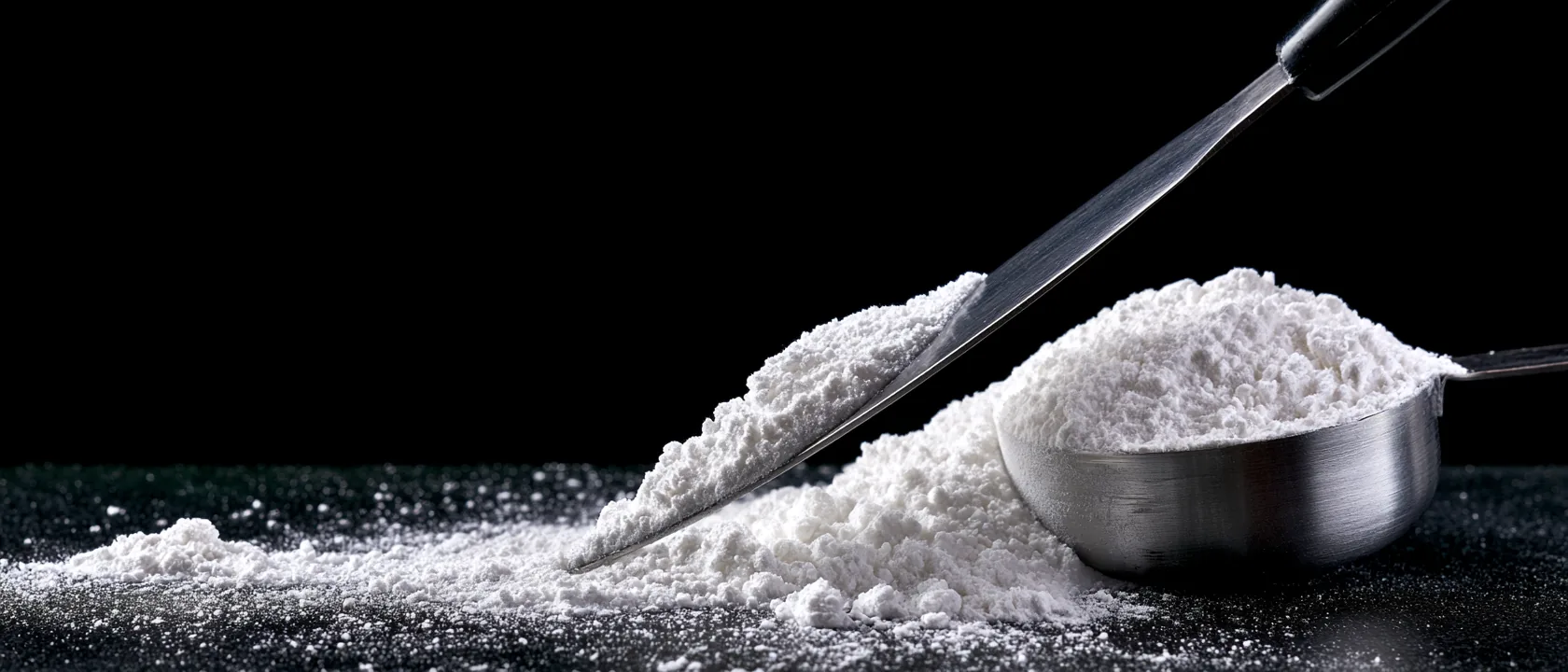 Macro photograph of a blade leveling white creatine powder across a steel measuring scoop